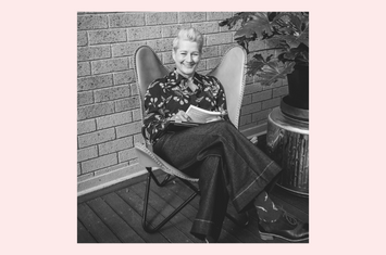 Susan Eldridge sitting on a chair with book in her hand laughing.